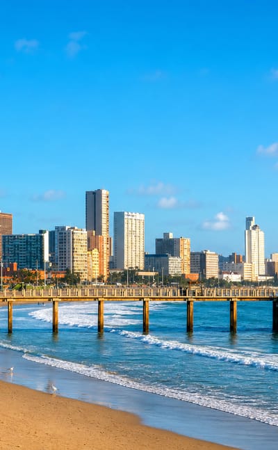 Durban's Golden Mile beachfront skyline behind a wooden pier and breaking Indian Ocean surf.