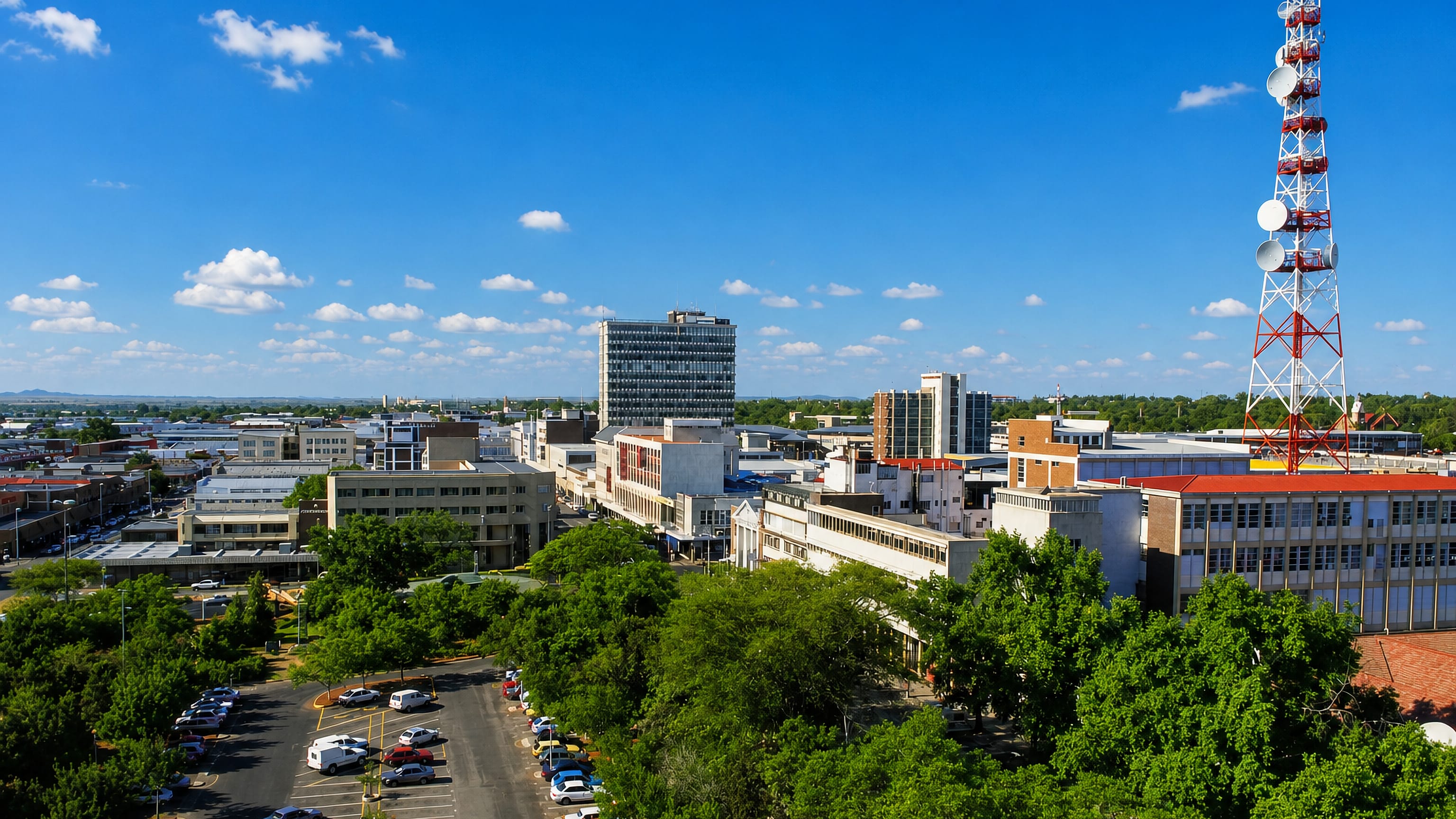 Polokwane's central business district under blue sky, with a red-and-white telecom tower rising above leafy streets.
