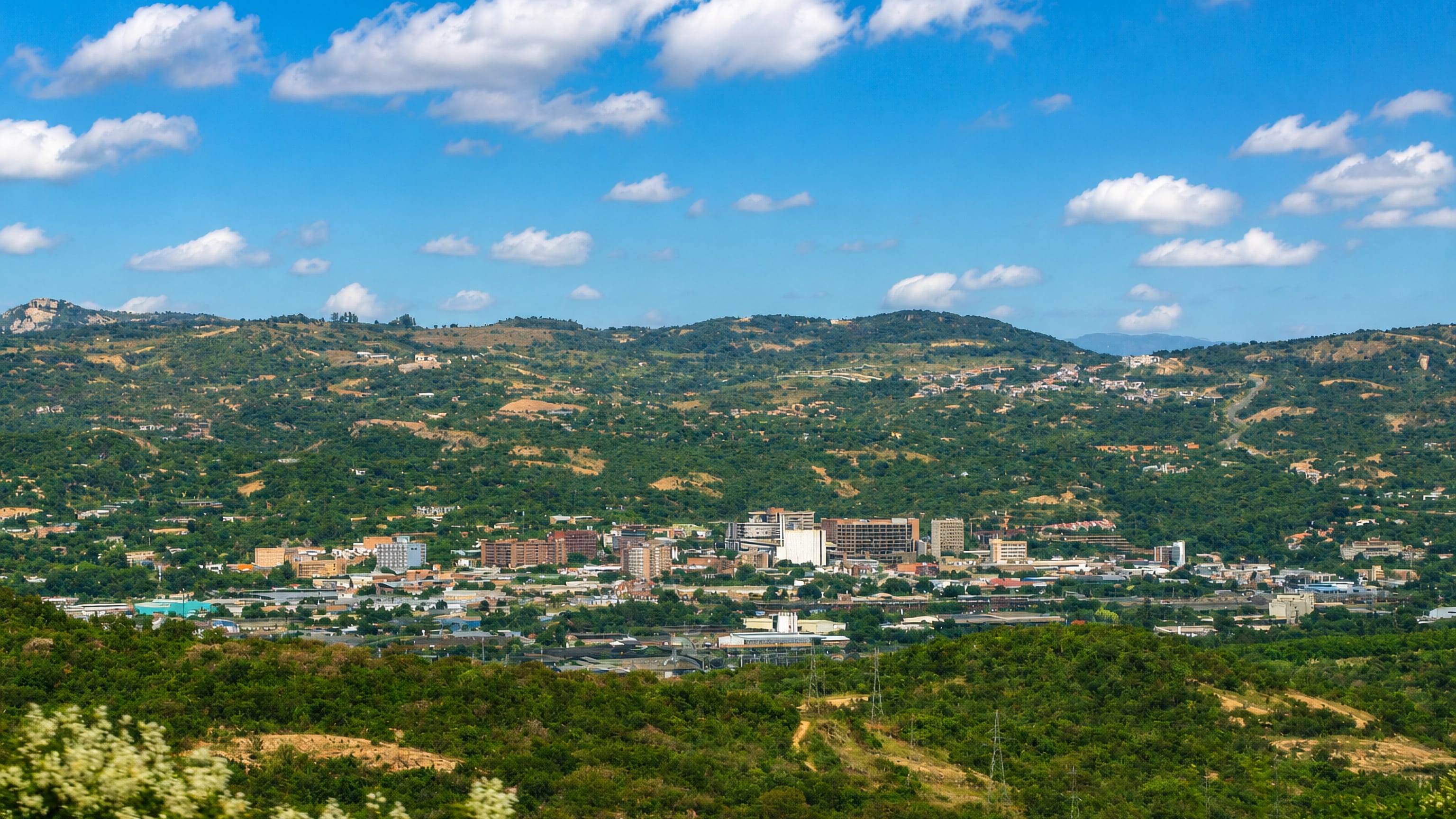 Mbombela set in a green Lowveld valley, its low-rise centre ringed by bush-covered hills under a blue sky.