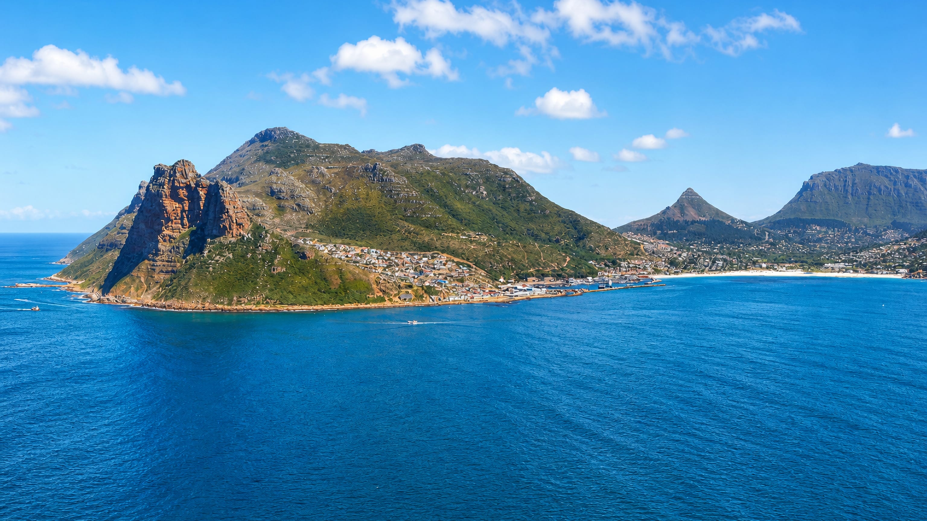 Hout Bay's harbour village below the Sentinel peak, with Cape Town's Lion's Head and Table Mountain across the bay.