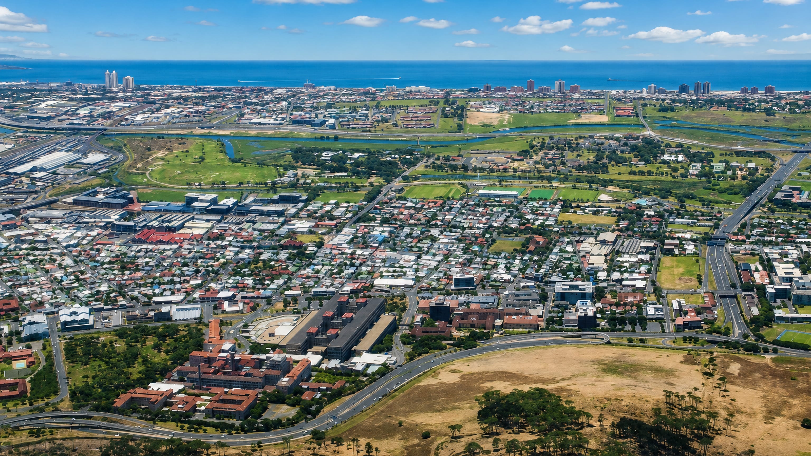 Aerial view across Observatory, Cape Town, with its hospital campus, street grid and Table Bay beyond.