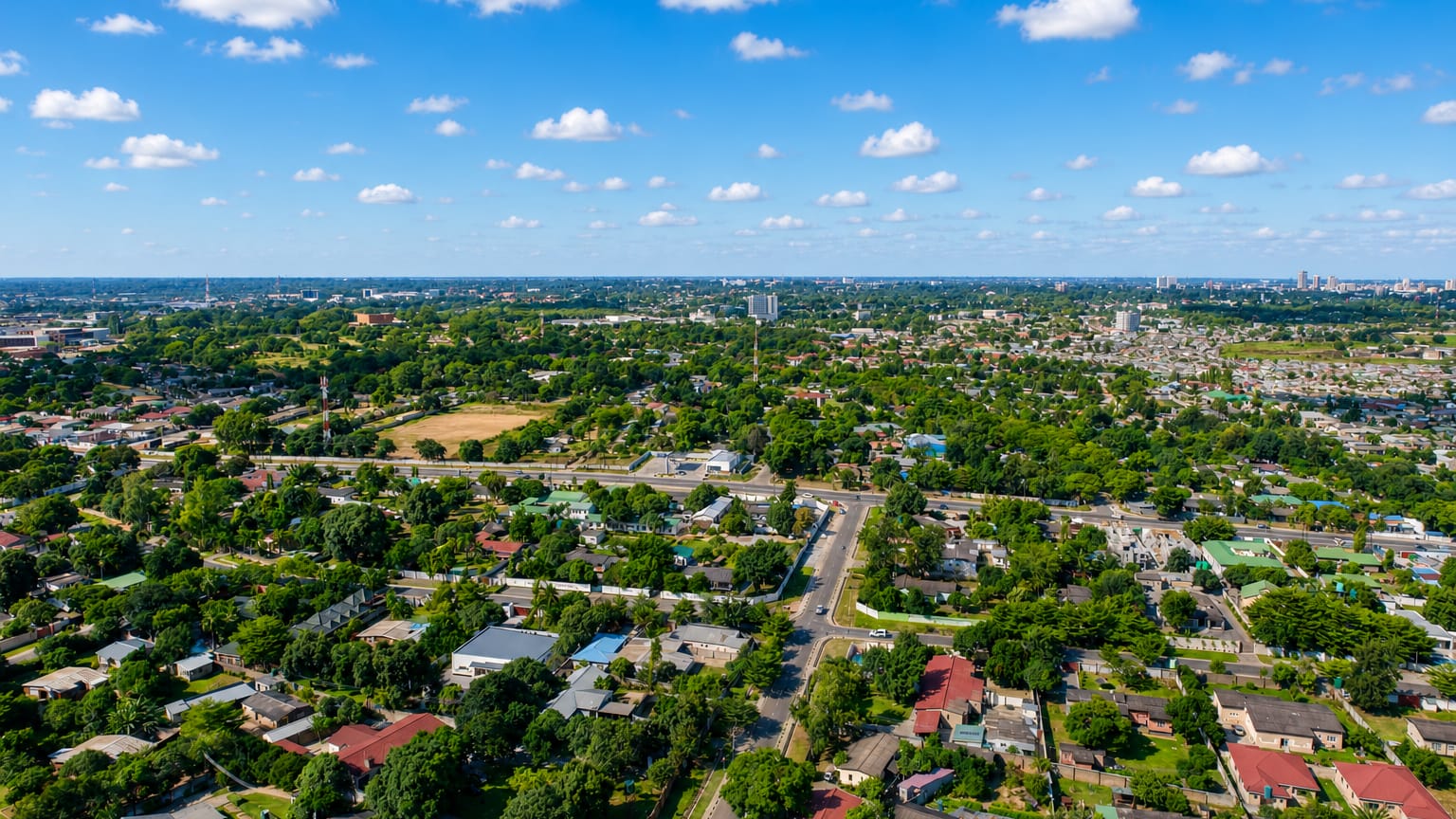 Aerial view of Lusaka's leafy low-rise suburbs and tree-lined avenues under a blue sky.