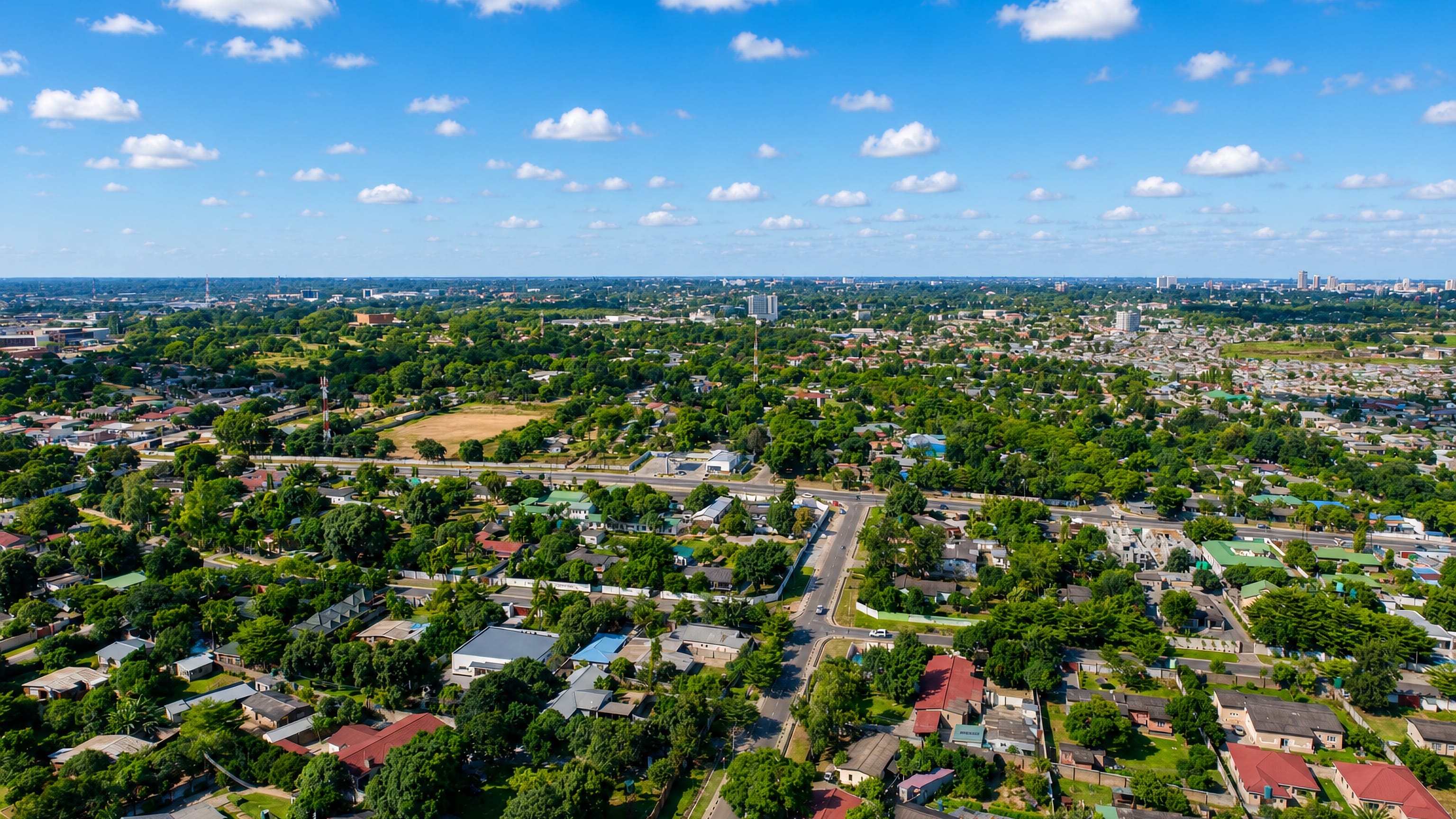 Aerial view of Lusaka's leafy low-rise suburbs and tree-lined avenues under a blue sky.