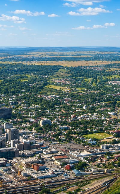 Aerial view of Harare, Zimbabwe, its low-rise city centre spreading toward green countryside under a blue sky.