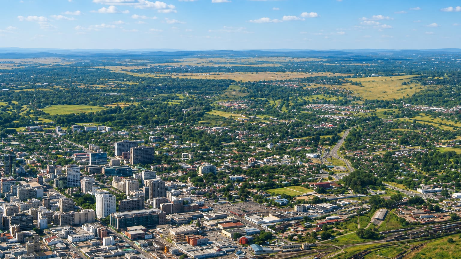 Aerial view of Harare, Zimbabwe, its low-rise city centre spreading toward green countryside under a blue sky.